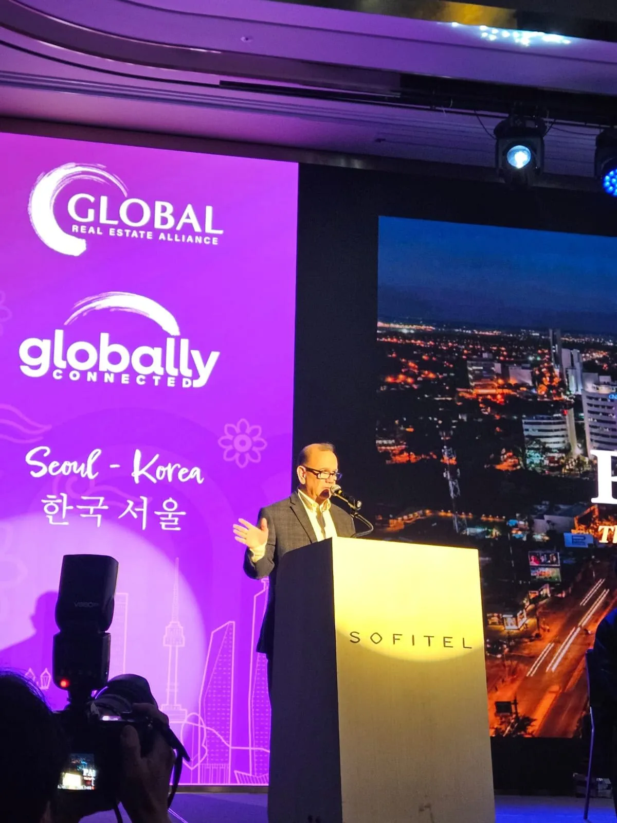 Kiko speaking at a podium in front of a large screen at an event in Seoul