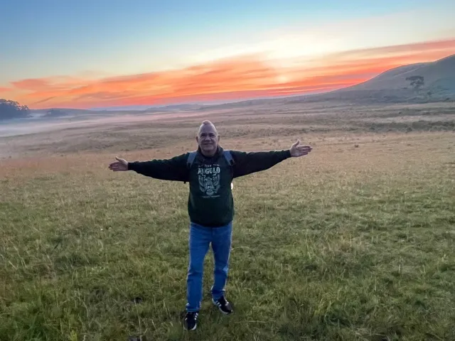 Kiko standing in a field at sunrise with his arms wide open