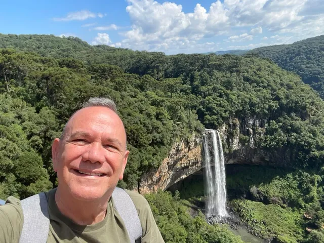 Kiko smiling in front of a waterfall in a forested canyon